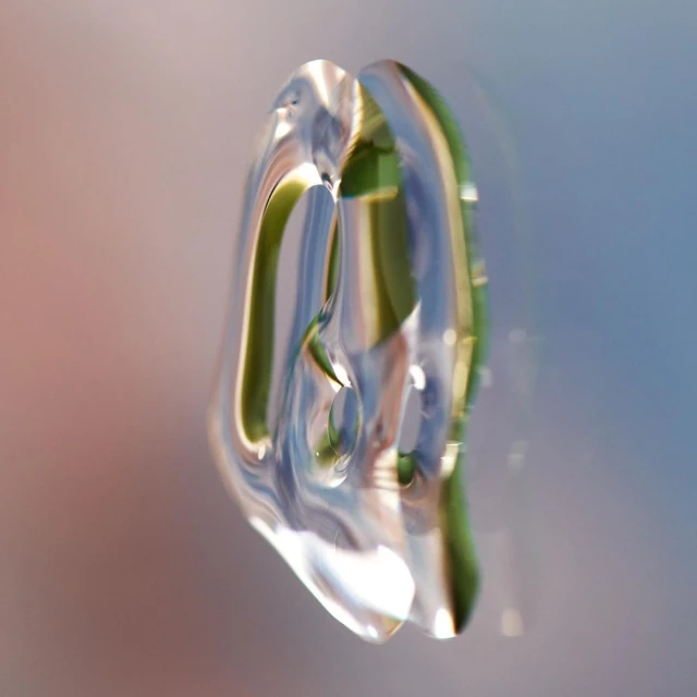 Abstract close-up of a clear, translucent object with green and blue reflections, set against a background gradient of peach and blue.