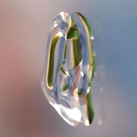 Abstract close-up of a clear, translucent object with green and blue reflections, set against a background gradient of peach and blue.