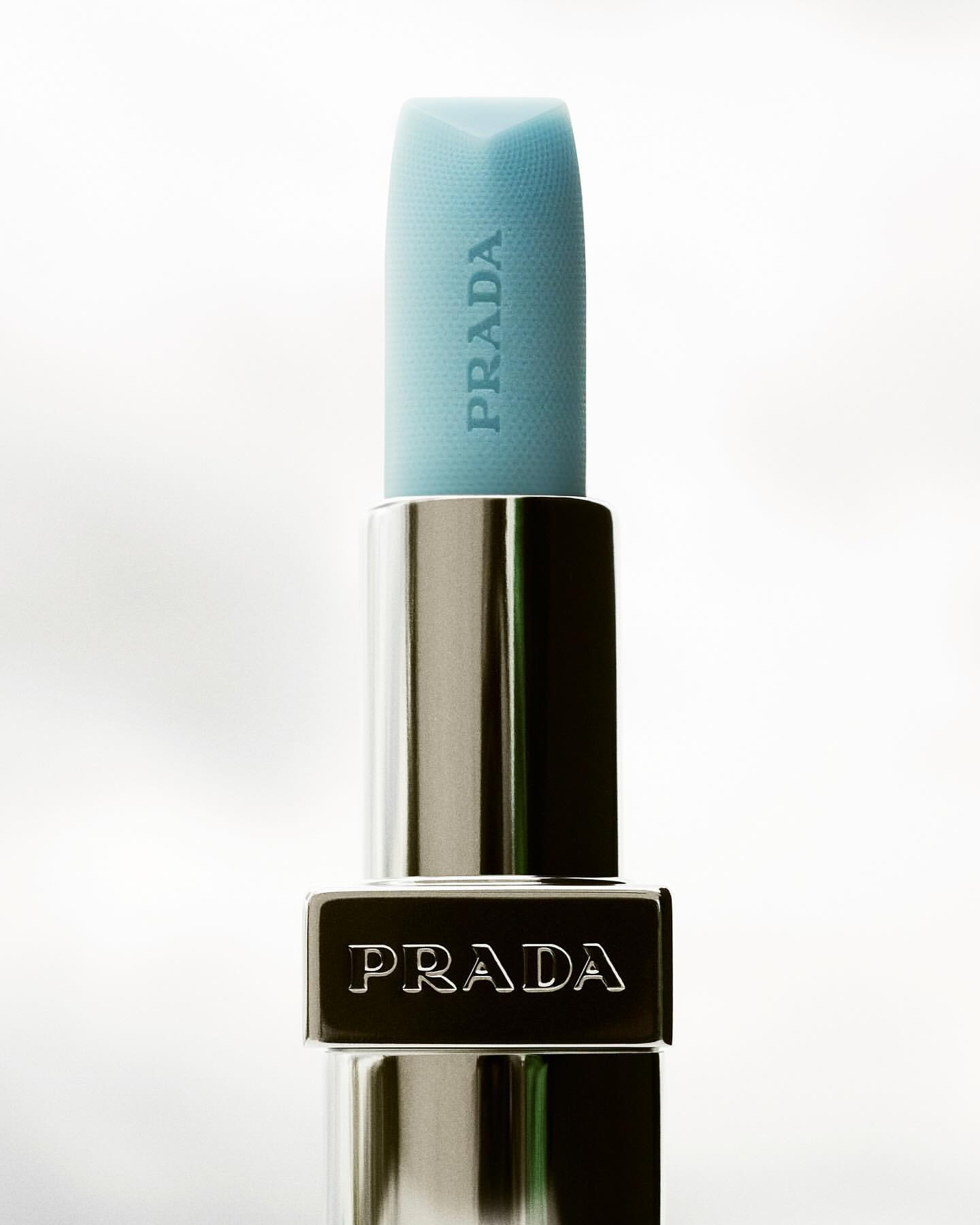 Prada lipstick close-up shot on a white background. The lipstick is light blue. The product design is simple, modern, and luxurious.