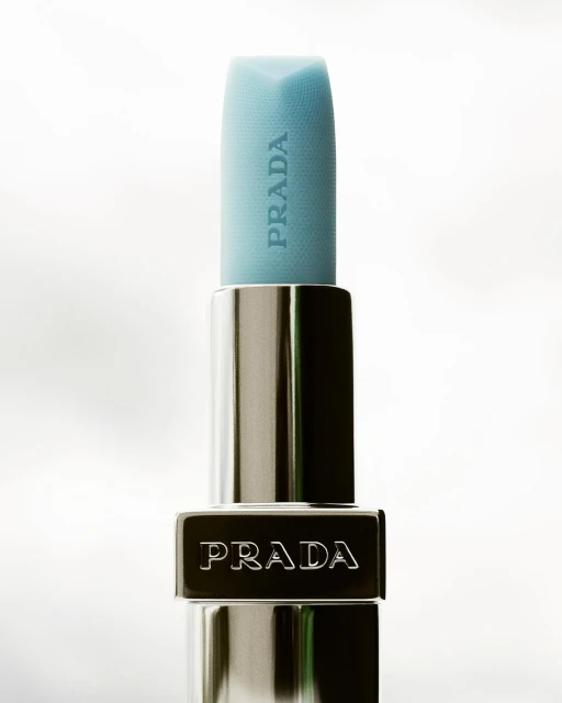 Prada lipstick close-up shot on a white background. The lipstick is light blue. The product design is simple, modern, and luxurious.