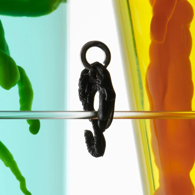 Close-up of a black ornate hook suspended by a metal rod with a colorful, abstract background featuring green, orange, and blue hues.