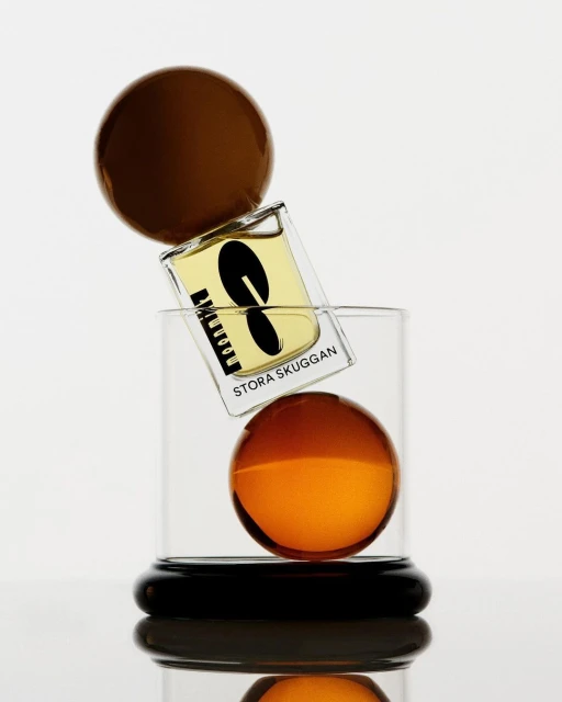 Still life shot of a perfume bottle balanced between two brown glass spheres against a bright white background in a studio setting.