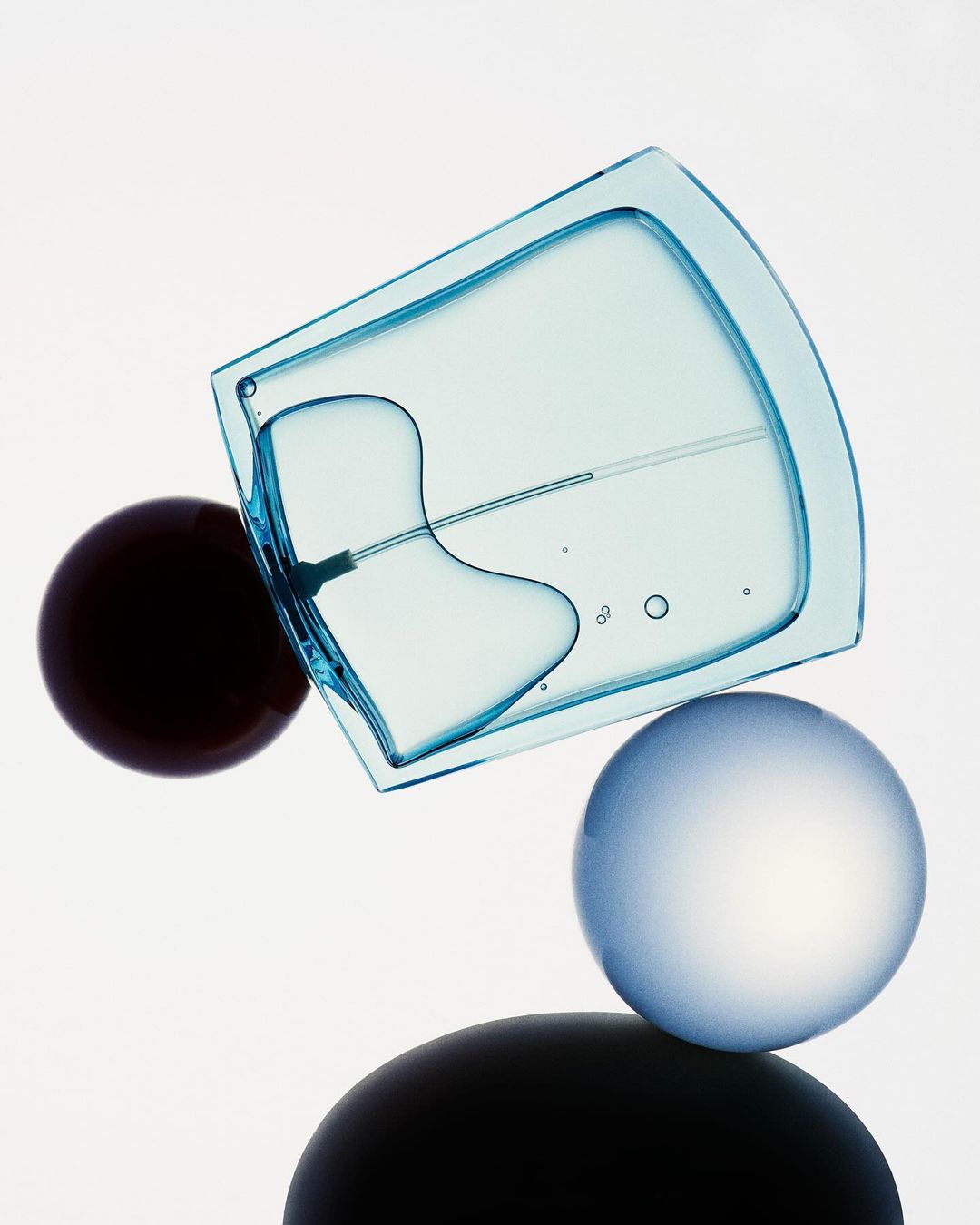 Blue glass perfume bottle angled over spherical spheres against a white background