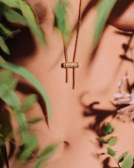 Elegant close-up of a woman's torso wearing a gold braided pendant necklace amidst blurred green foliage for a natural aesthetic.