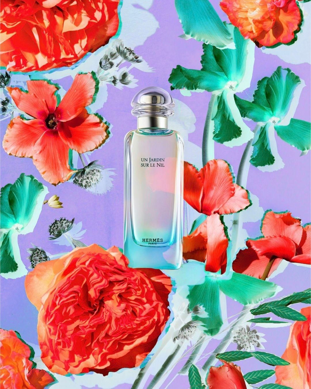 Close-up studio shot of a perfume bottle from Hermes, titled 'Un Jardin Sur Le Nil,' surrounded by an arrangement of bright flowers.