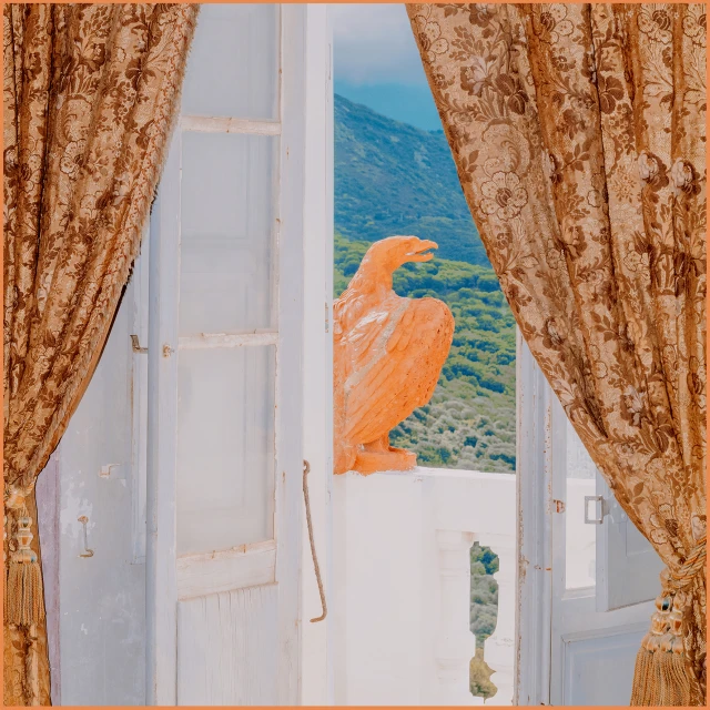 Open white french doors reveal a light orange eagle statue overlooking the mountain landscape, framed by patterned brown curtains.