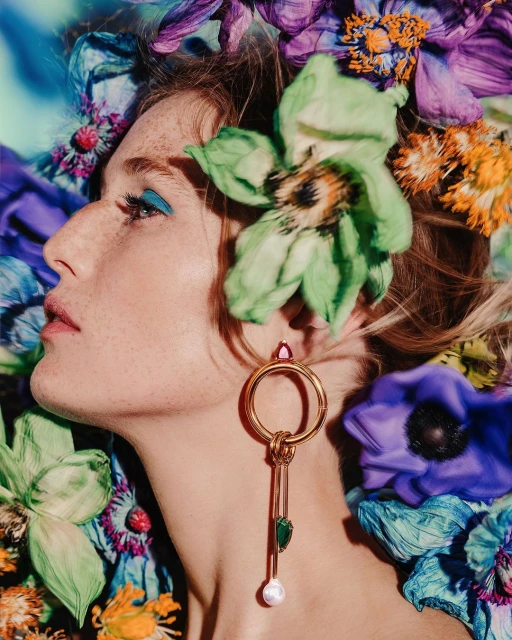 Profile view of a woman surrounded by flowers with artistic makeup, gold earring, and fair skin, showcasing beauty and floral design.
