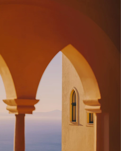 Architectural view through arched openings featuring ocean and distant mountains, bathed in warm, soft light during daytime.