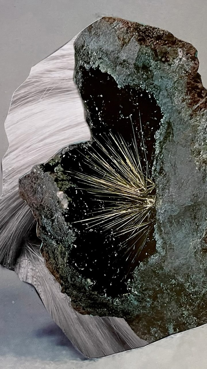 Close-up of a geode featuring a dark mineral exterior and interior filled with thin, radiating crystalline formations.