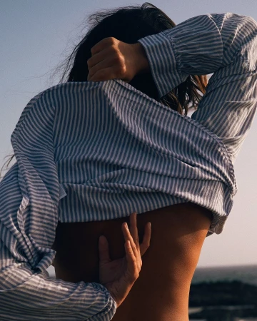 Back view of a slender adult woman in a striped shirt with her hand gently touching her back outdoors during daytime.