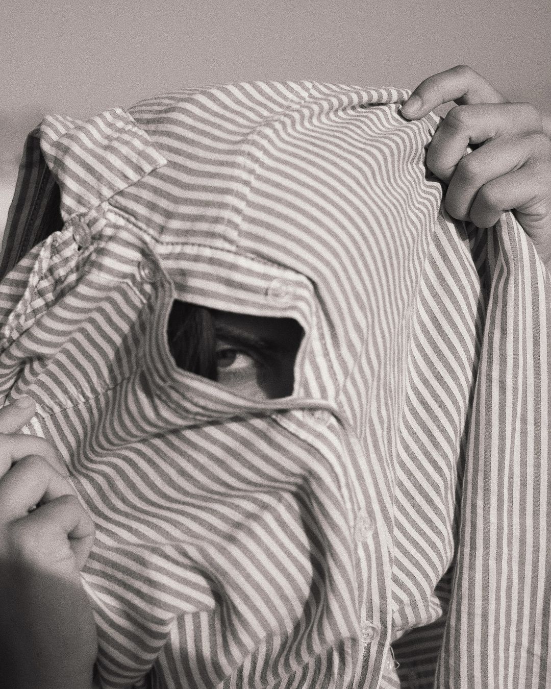Monochromatic portrait of an individual peering through a hole in a striped shirt, creating a unique and mysterious visual composition.