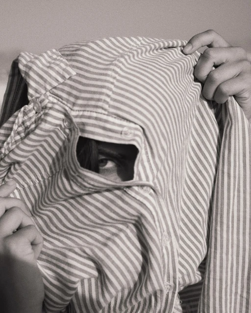 Monochromatic portrait of an individual peering through a hole in a striped shirt, creating a unique and mysterious visual composition.