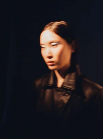 Close-up portrait of a woman with dark hair wearing a black leather jacket against a dark background, photographed by Linda Ambrosius.