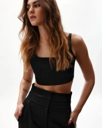 Portrait of a woman wearing a black crop top and black trousers against a plain white background