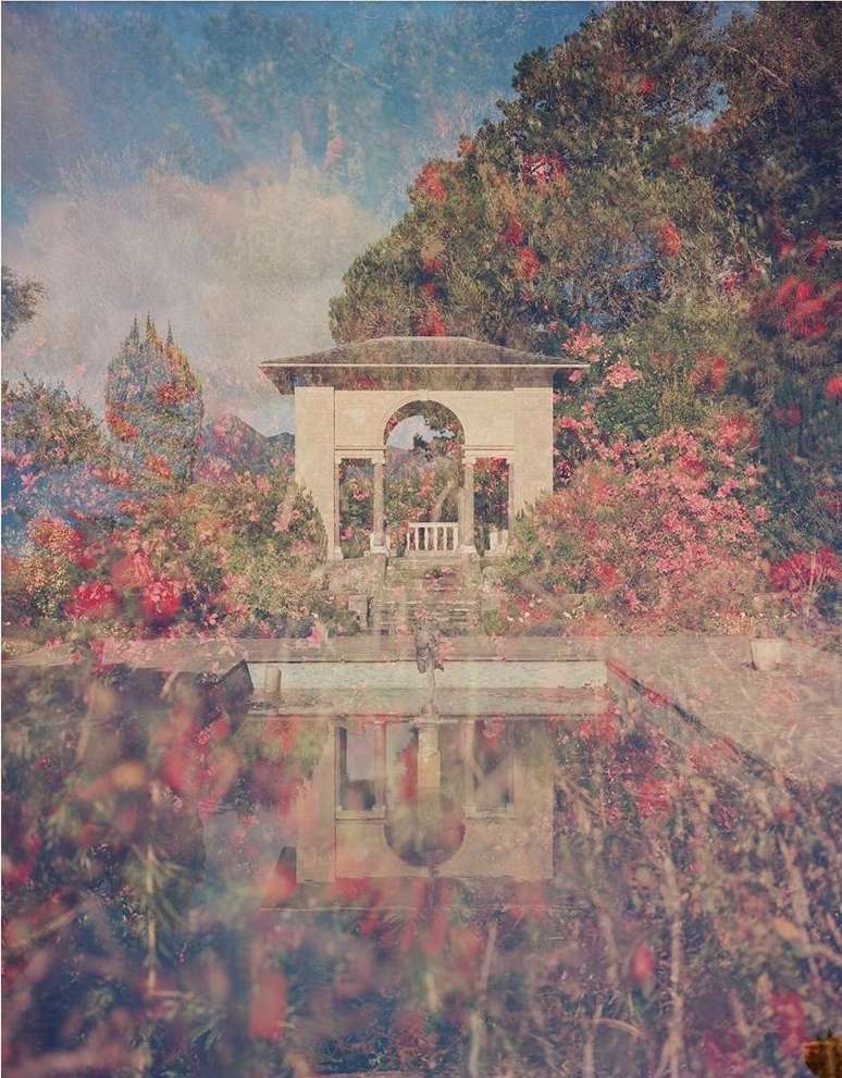 Architectural gazebo reflected in a pool, surrounded by flowering shrubs and trees under a bright, partly cloudy sky.