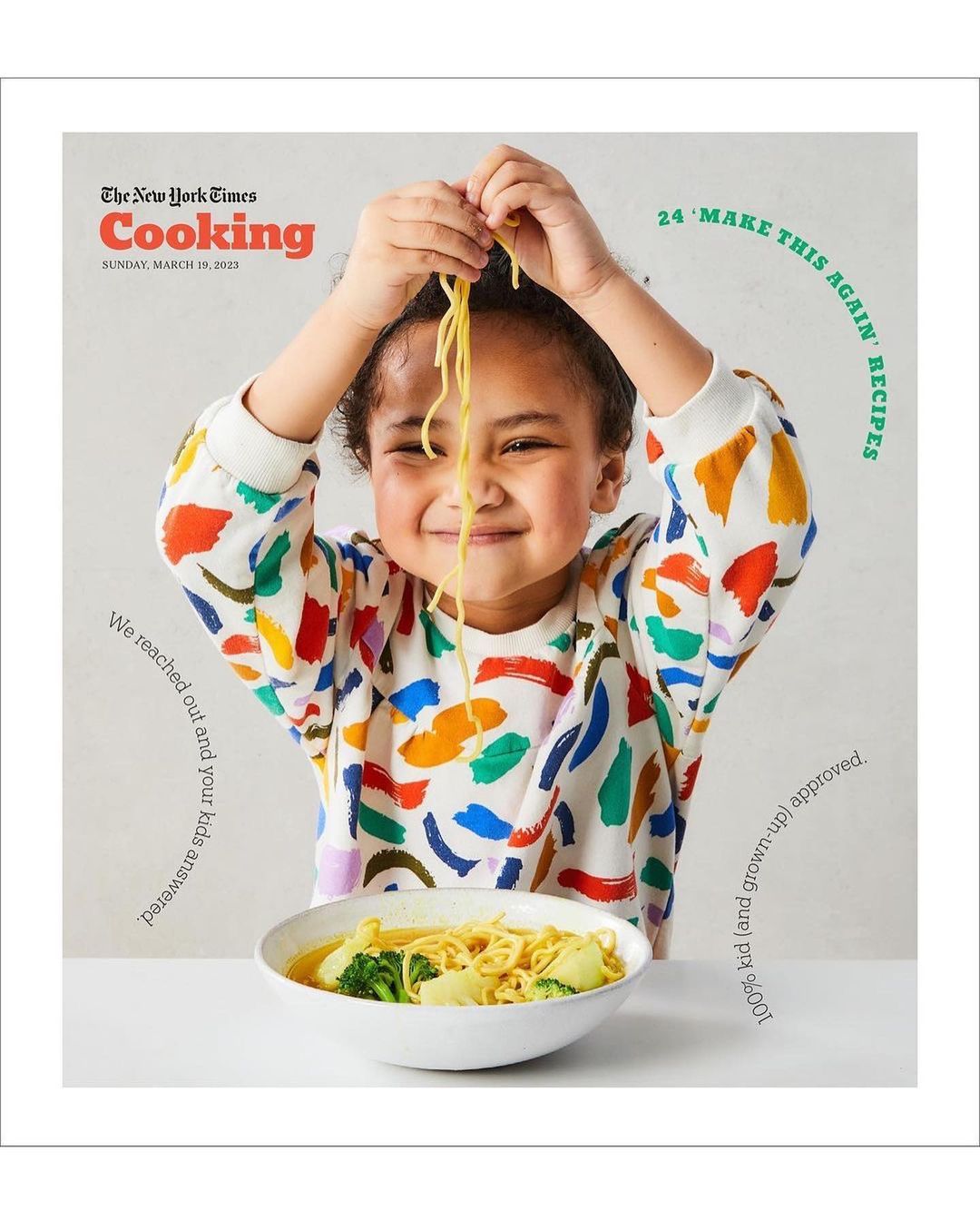 A young child with a bright, patterned shirt smiles while holding spaghetti over a bowl of noodles and broth on a cooking magazine cover.