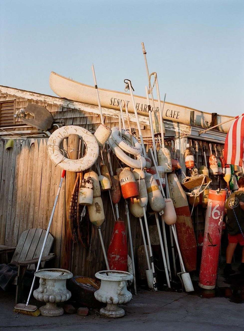 Outdoor display of colorful buoys, white life preservers, and a canoe above the Seaport Harbor Cafe creates a nautical scene.