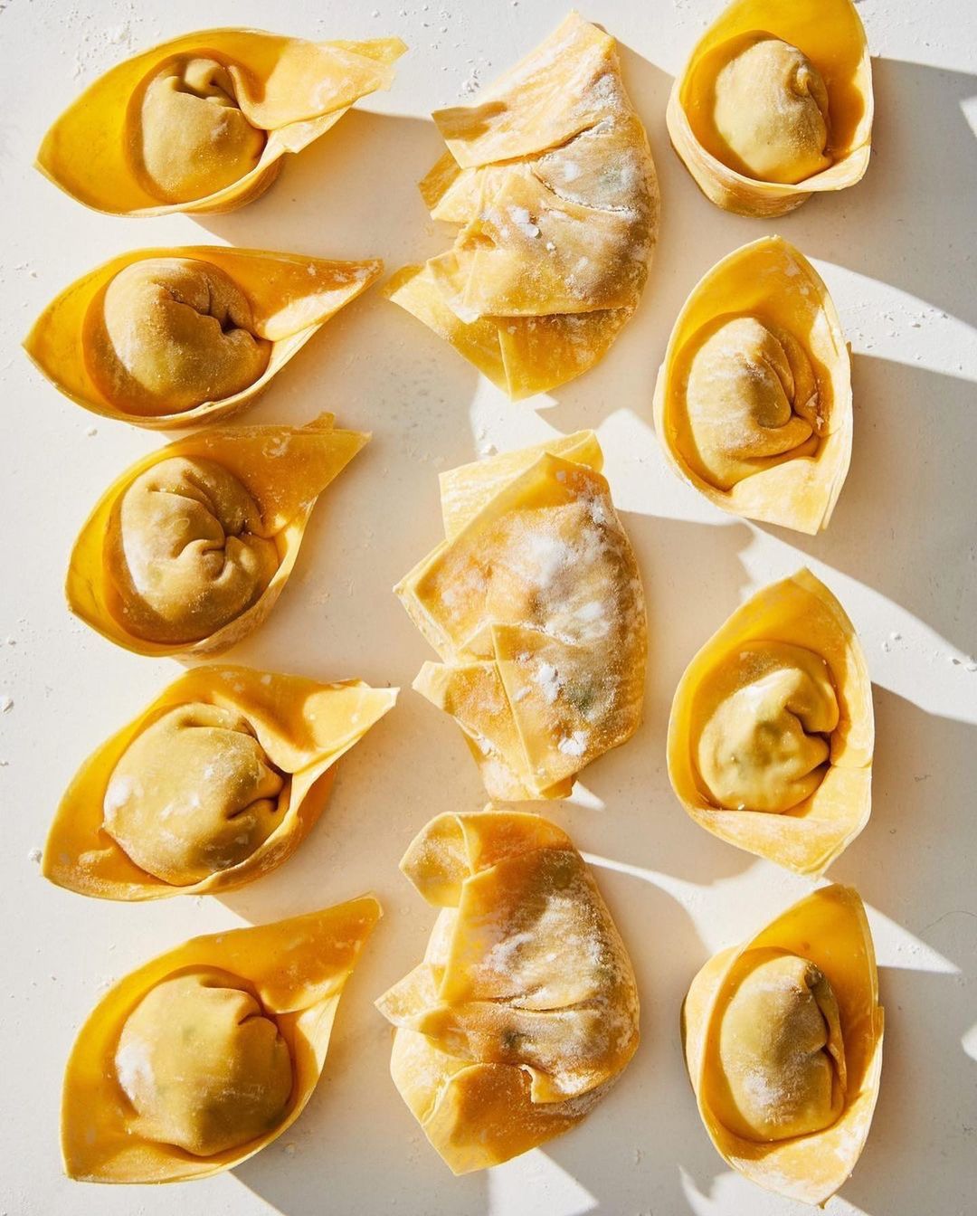 Overhead shot of several wontons arranged on a white surface, some with filling exposed and others as flat sheets.
