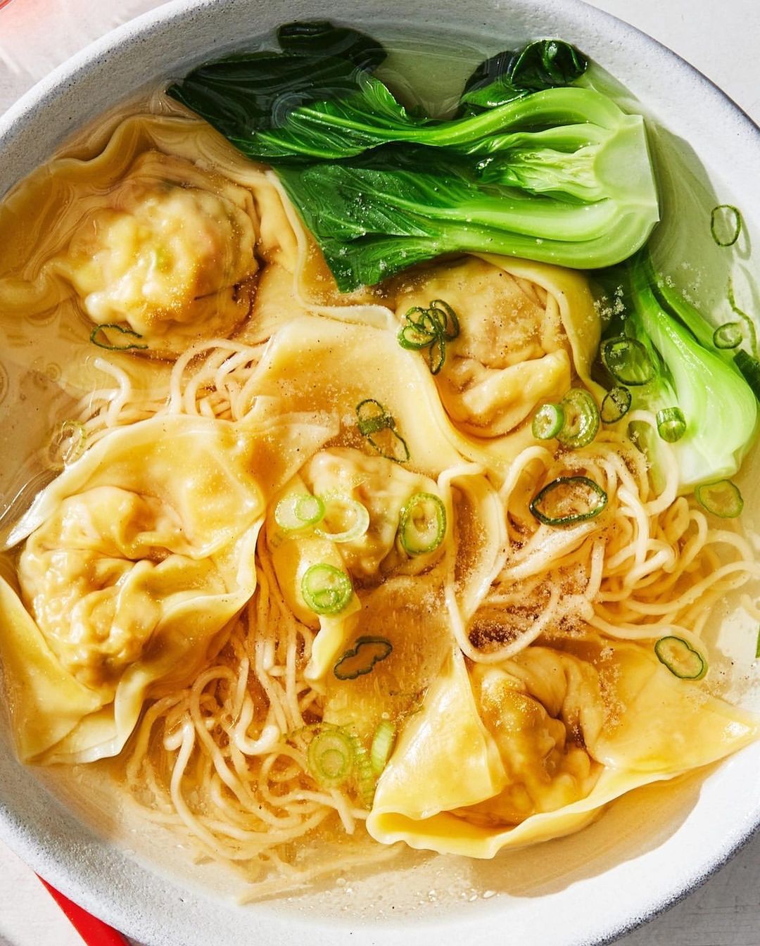 Overhead view of wonton noodle soup with bok choy in a white ceramic bowl, showcasing a culinary still life, food photography.