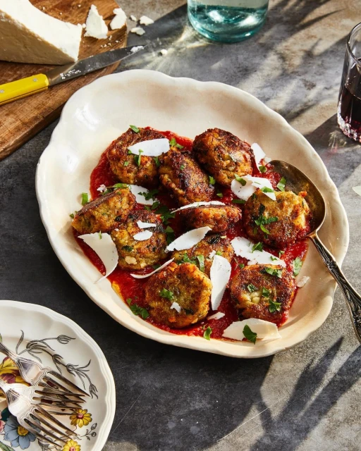 Overhead shot of a plate of meatballs in red sauce with cheese, garnished with parsley, alongside a glass of wine and cheese.