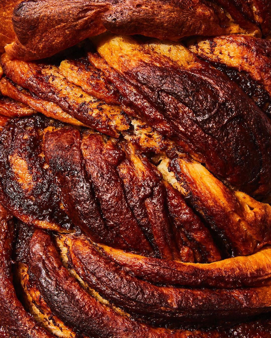 Close-up photograph of a baked babka bread loaf showcasing its layered swirls and dark golden crust with a textured surface.