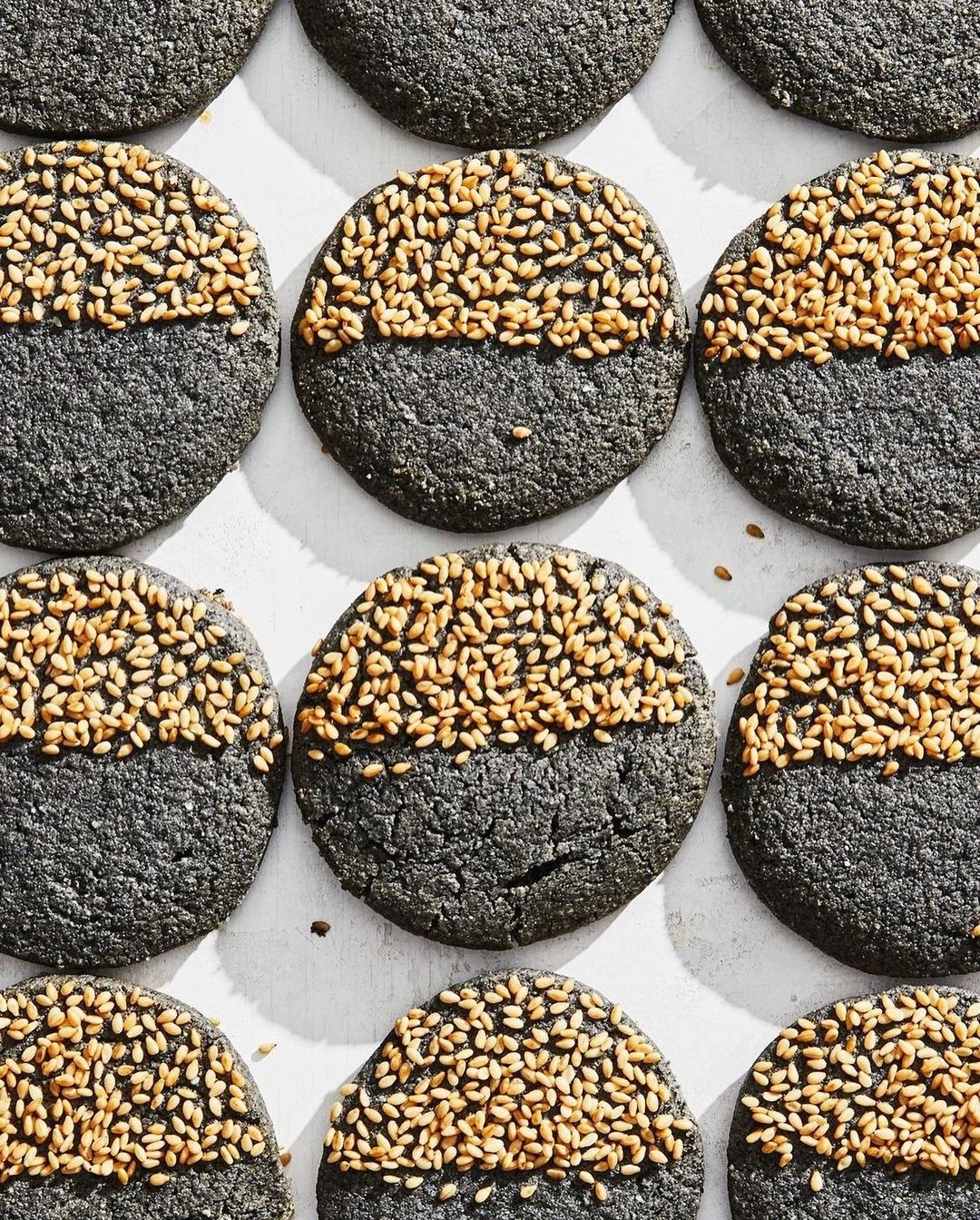 Overhead food photography by Linda Xiao of round black cookies decorated with a top crust of golden sesame seeds.