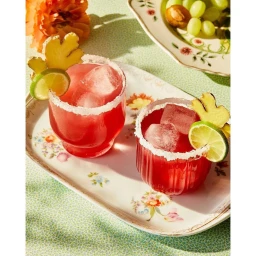Two red cocktails in sugar-rimmed glasses with lime and ginger garnishes on a floral tray, photographed by Linda Xiao.