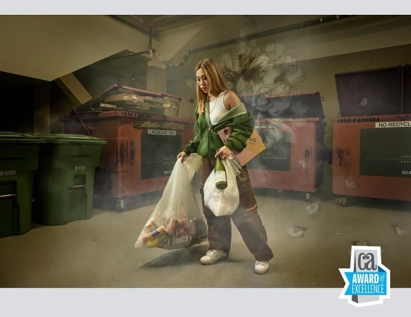A young woman carrying a plastic bag filled with recyclable items, standing in front of large recycling containers in an indoor environment.