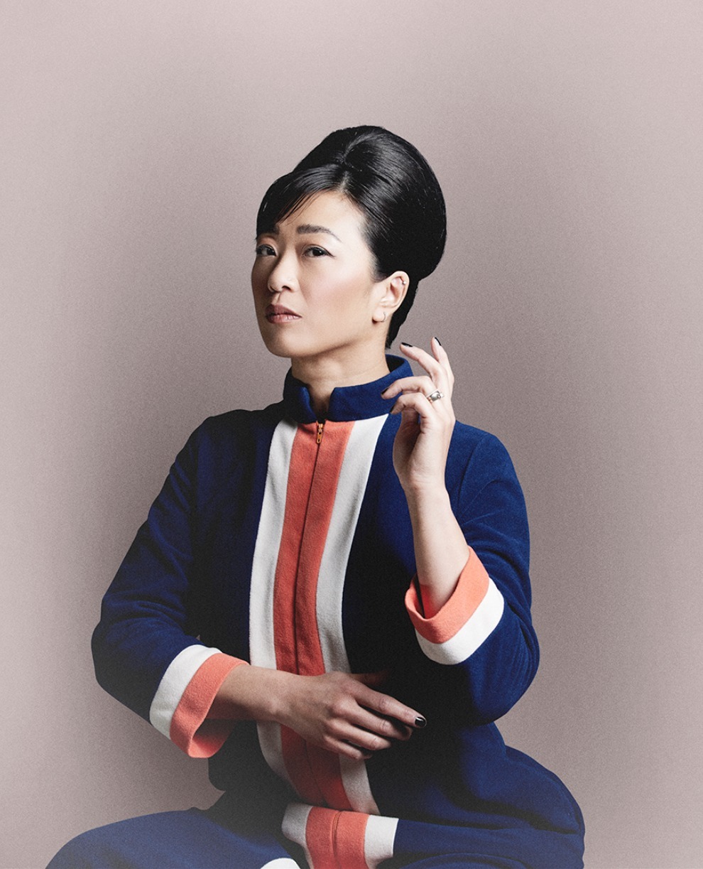 Adult woman with dark hair in retro style posing indoors wearing a blue and orange dress in a portrait-style photograph.