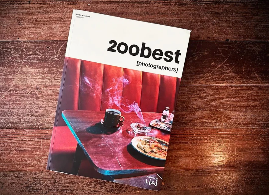 Coffee cup, ashtray, and half-eaten meal are displayed on book cover on a wood surface, featuring a red vinyl booth backdrop.