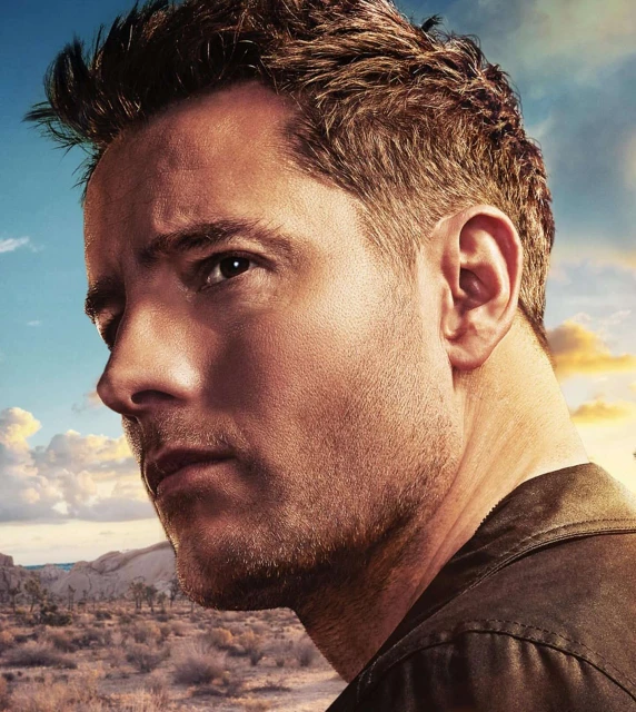Close-up portrait of an adult male with short brown hair and stubble, wearing a collared shirt, set against a soft desert background.