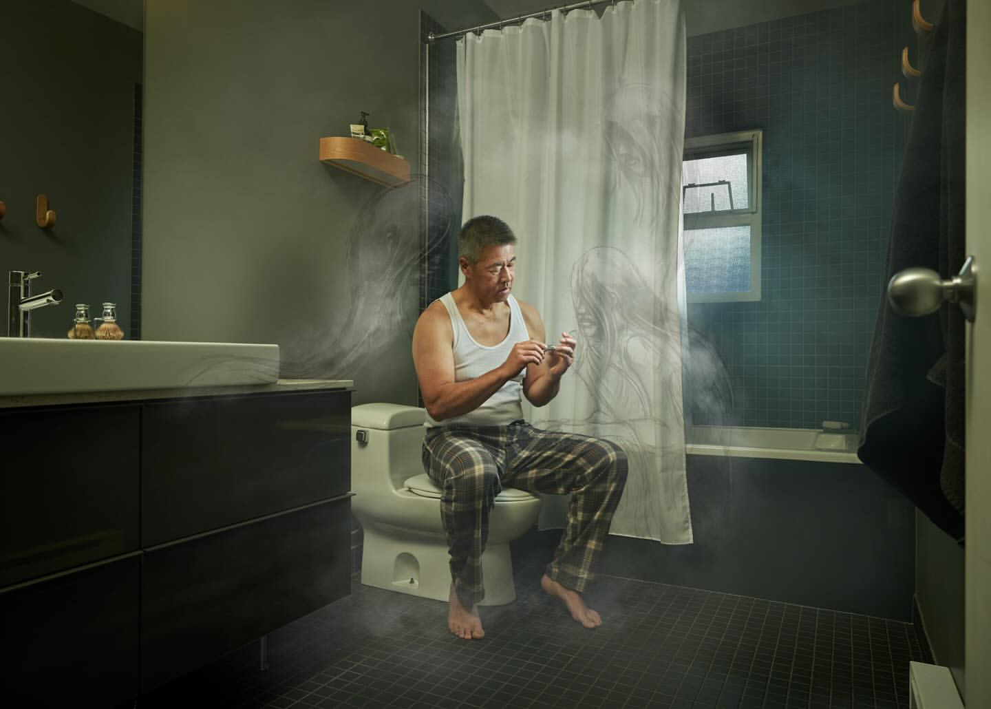 Mature man in pajamas sits in a dimly lit bathroom, his gaze fixed on his hands as he prepares to clip his fingernails.