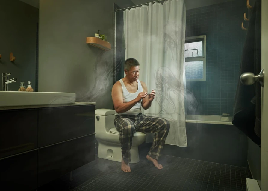 Mature man in pajamas sits in a dimly lit bathroom, his gaze fixed on his hands as he prepares to clip his fingernails.