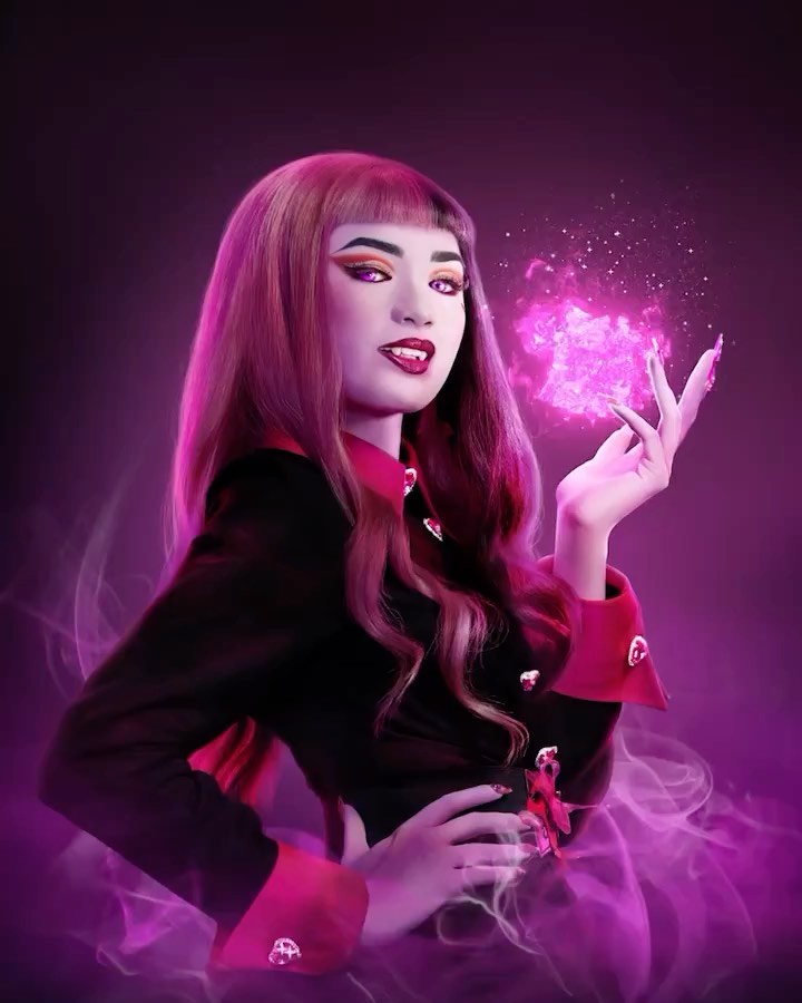 A woman with pink hair wearing a black and red outfit holds a glowing pink cube in front of a dark purple background.