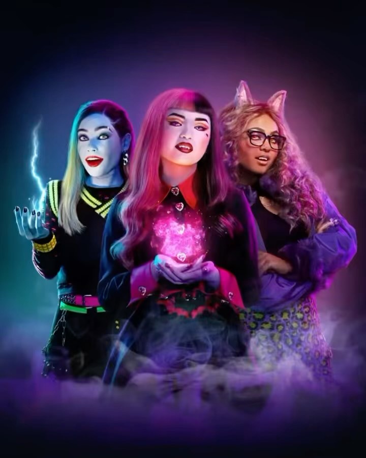 Three adults in Monster High-themed costumes, one casting a magic spell, in a fantasy studio setting with vibrant colors and fog effects.