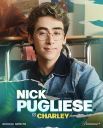 Portrait of young man wearing round glasses and denim jacket seated in a classroom setting