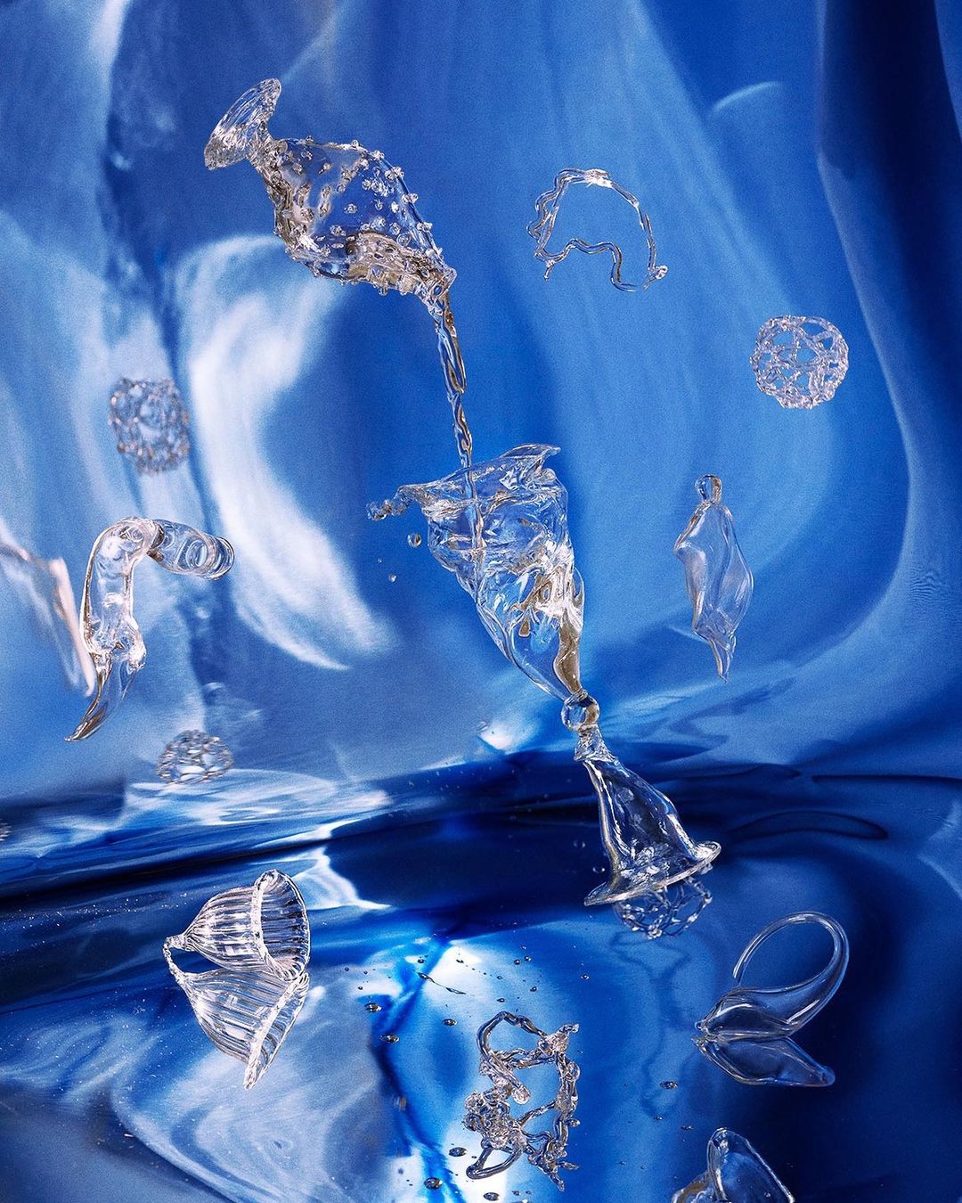 Abstract still life of water pouring between clear glasses, captured with dramatic lighting and set against a blue background.