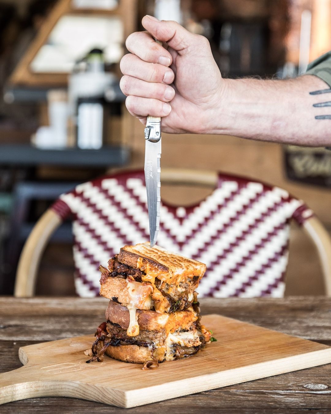 Overstuffed sandwich on wooden board with knife. Grilled cheese on sourdough piled high with meat and cheese filling.