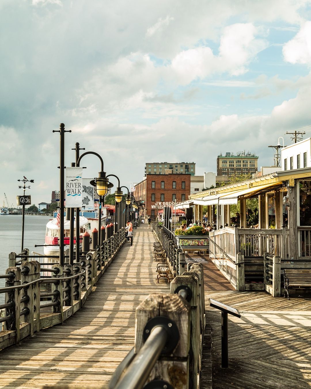 Scenic view of River Walk in Savannah, Georgia, showcasing a charming boardwalk lined with benches, lamp posts, and historic buildings.