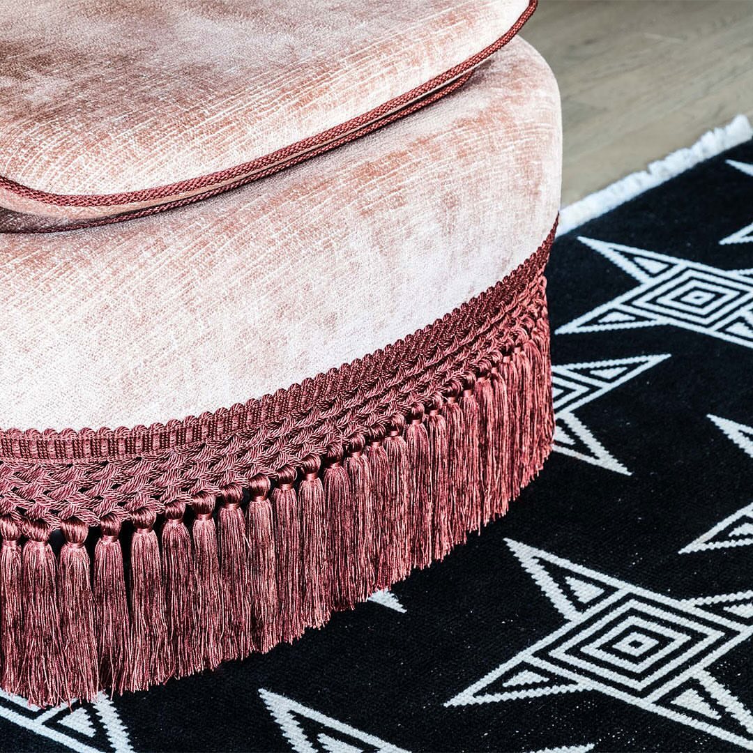Interior design detail featuring a pink velvet upholstered ottoman with tassel trim alongside a black and white patterned rug.