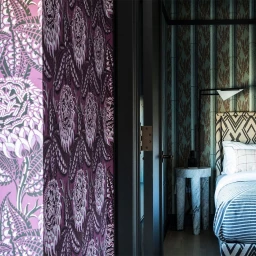 Interior bedroom view framed by a dark doorway with purple patterned wallpaper in the foreground by Lisa Corson