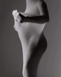 Monochrome studio portrait of a person wrapped in translucent stretchy fabric, pulling it taut near the chest.