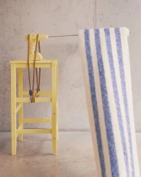 A yellow power drill mounted on a yellow wooden stool with a large striped textile hanging vertically from a metal rod.