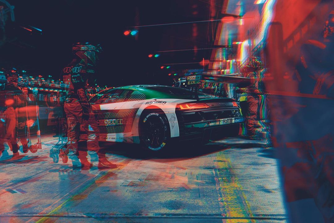 Race car at pit stop, refelctive light display, person on the left holding a roller board, tire visible at the bottom.