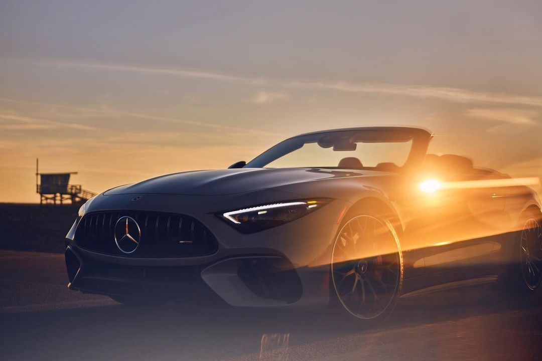 Sleek grey convertible car parked at dusk, with a beach lifeguard tower visible in the background under a golden sunset sky.