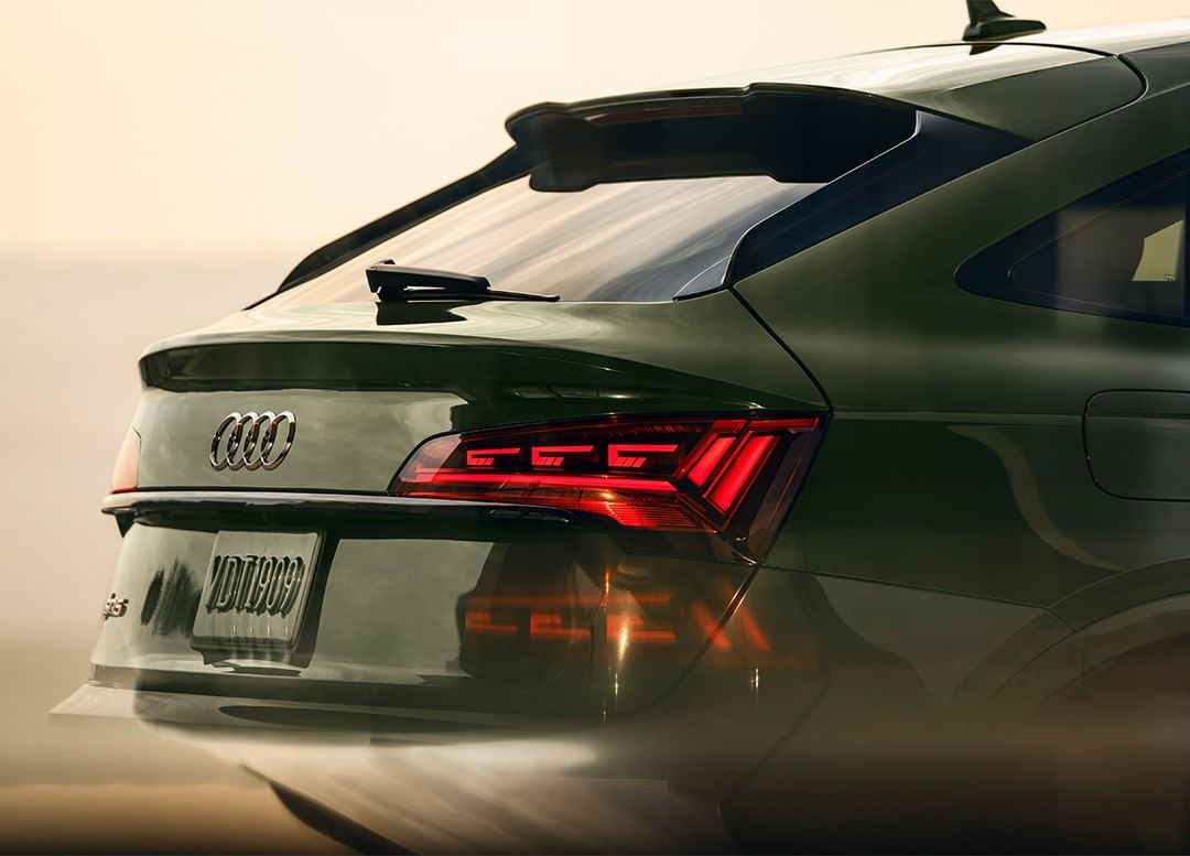Close-up of the rear of a dark green Audi Q5 Sportback, showcasing its taillights, Audi logo, and license plate against a light background.