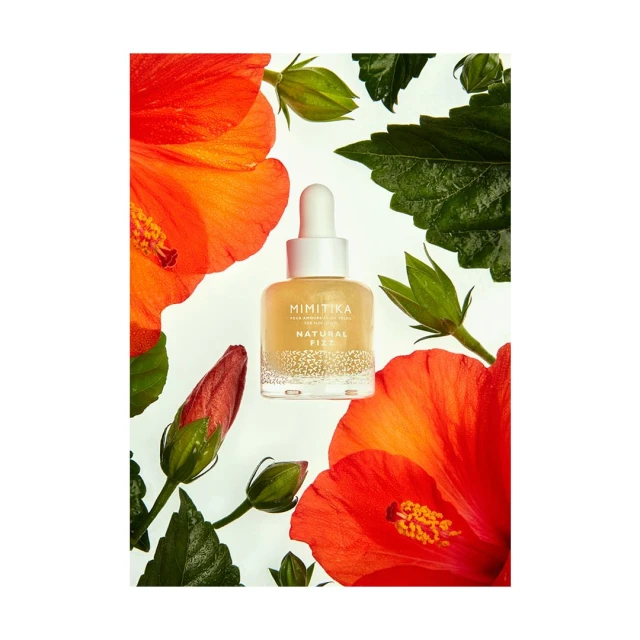 Mimikitka Natural Fizz bottle surrounded by red and orange hibiscus flowers and green leaves on a white background for beauty content.
