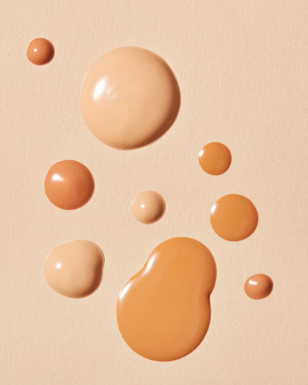 Close-up studio shot of different shades of foundation drops on a neutral background, highlighting a beauty and makeup theme.