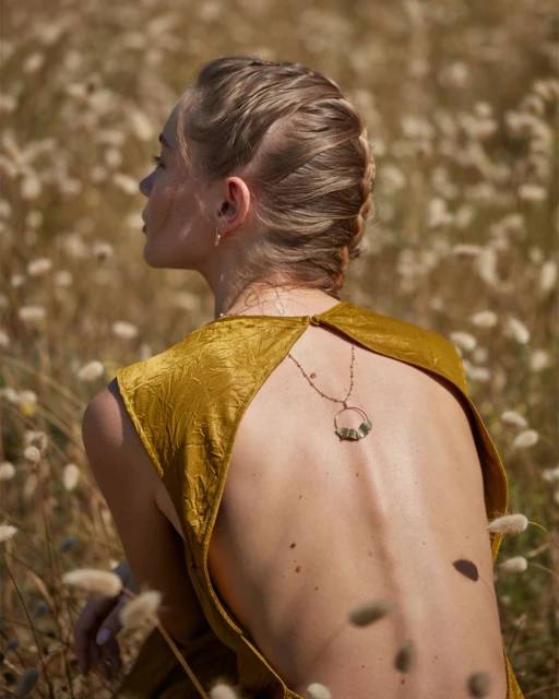 Woman in golden dress with open back and braided hair kneeling in field of ornamental grasses. Golden light, outdoor fashion.