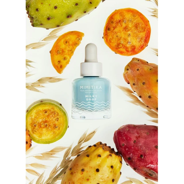 Serum bottle surrounded by colorful prickly pear fruit and wheat stalks, set against a clean white background in a beauty product shot.
